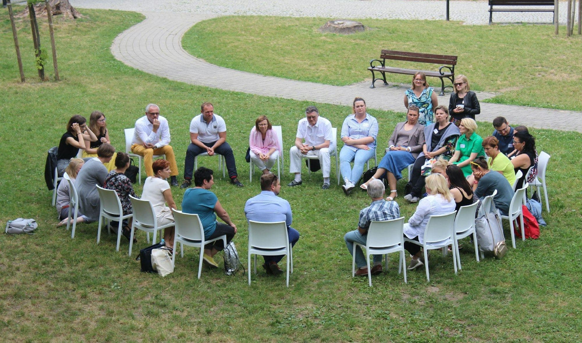 A community assembly seated in a circle of chairs on a lawn