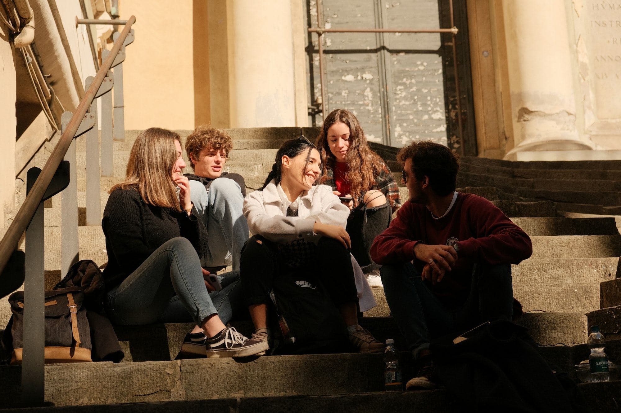 A group of students sitting and talking on sunlit stone steps