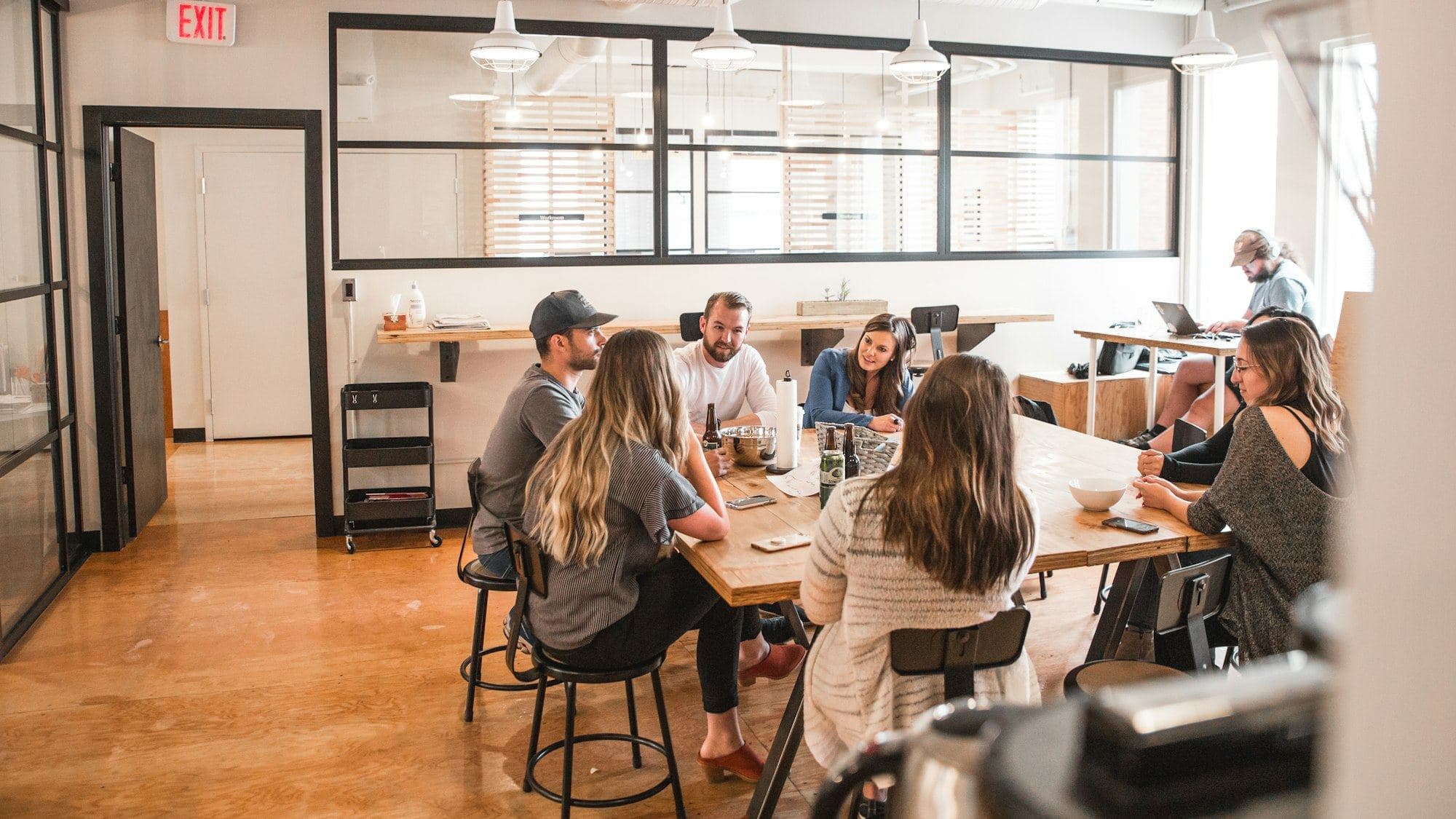 A team in discussion around a long wooden table in a bright workspace